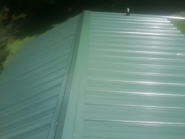 New green metal panels meeting at the ridge of a roof — Flat Roof Repair work by our crew in Orland Park