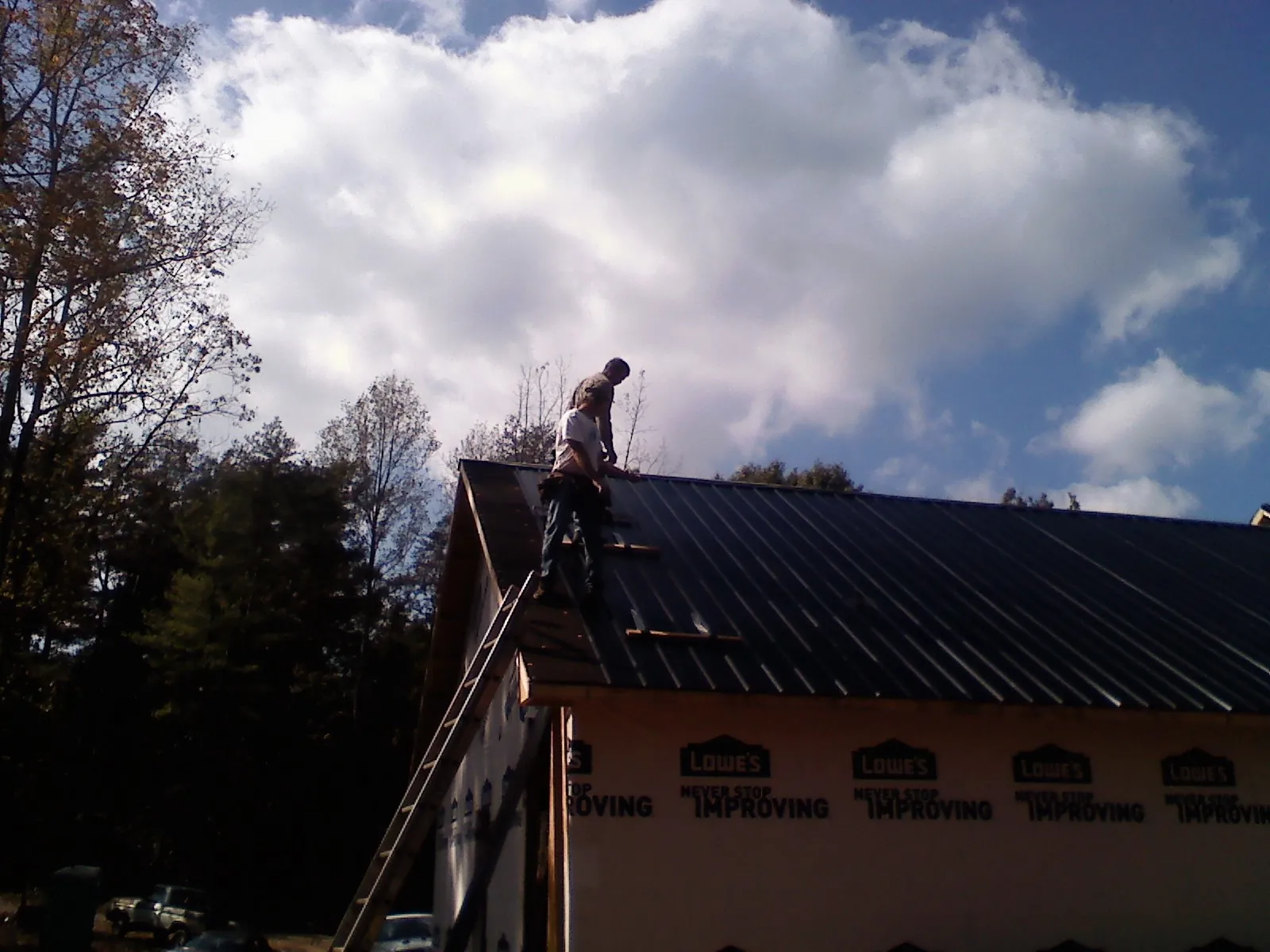 Roofer fastening dark metal panels high against a cloudy sky, from a Roof Inspection job in Orland Park