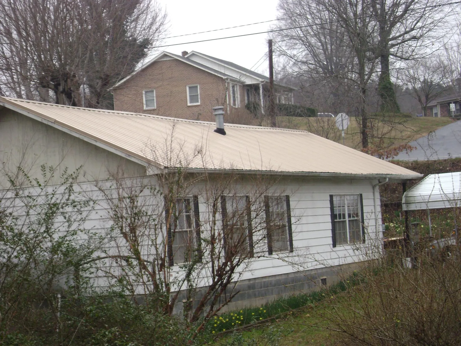 Tan metal roof on a white sided house set into a hillside — Commercial Roofing by Roofing Brothers in Orland Park